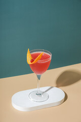 Pink alcoholic cocktail in steamed glasse on white podium or pedestal on colored background