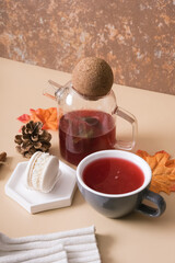 Cup and teapot with cranberry tea and macaroon with an autumn leaf. Autumn warm drink concept