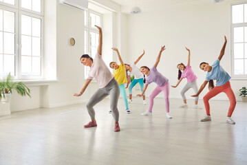 Children having a fitness dance workout. Kids doing sports exercises or dance moves with a professional trainer. Group of girl dancers in sportswear dancing together with a woman teacher at the gym