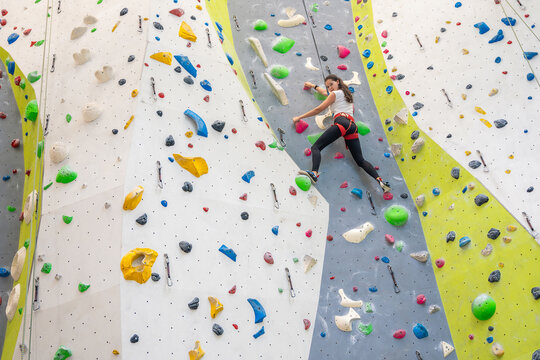 Rock climber young woman hanging on colored hooks on climbing artificial wall indoors of sport centre of Prague. Extreme sports and bouldering concept