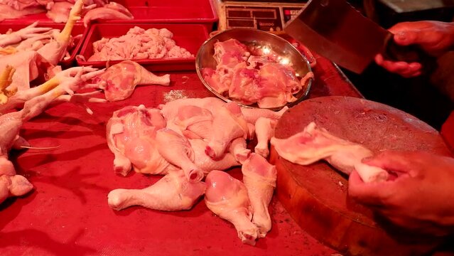 A seller of chicken meat in a traditional market at night who is serving customers, cutting and weighing the meat purchased.