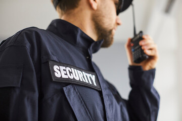 Close up cropped portrait of confident male security guard standing indoors. Bearded guardian man in blue uniform talking by the walkie talkie and looking to the side. Selective focus. - Powered by Adobe