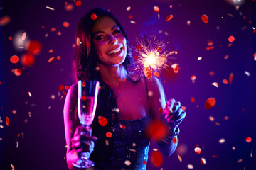 Portrait of a smiling woman, posing in front of a purple background, surrounded by confetti, holding a sprinkle.