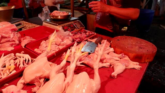 A seller of chicken meat in a traditional market at night who is serving customers, cutting and weighing the meat purchased.