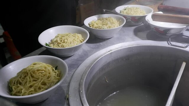 In the process of cooking Chicken Noodles, Indonesian street food, the chef prepares a bowl that has been added secret oil and mustard greens, then pours the cooked noodles into the bowl