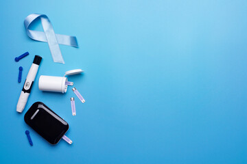 Diabetes awareness concept of ribbon glucose meter test strips and lancets on blue background flat lay