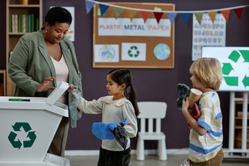 Side view portrait of little girl sorting plastic in recycling class at preschool, copy space