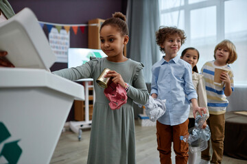 Side view portrait of Black little girl sorting plastic in recycling class at preschool, copy space