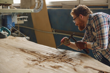 Professional craftsman working with chisel while cutting wooden plank in carpentry workshop