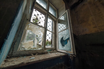 Opened window with shattered glass inside dark room of abandoned building in daytime