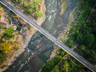 Aerial view of a large bridge built with sturdy and strong concrete pillars over the Progo River, Kulon Progo, Yogyakarta. Long bridge with rocky receding river and dried tropical forest backgrounds.
