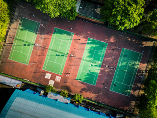 Aerial bird-eye view of a four private tennis court with green color and trees. People are...