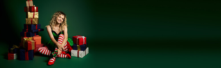 cheerful new year elf sitting with her legs crossed and posing next to pile of gifts, banner