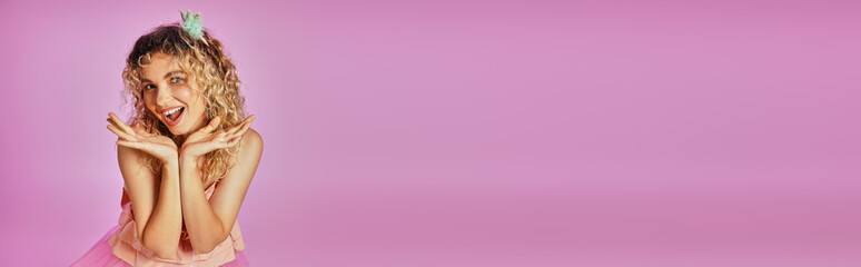 Obraz premium joyful pretty woman in pink tooth fairy costume smiling at camera with hands raised to face, banner