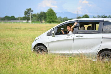 Joyful two young woman driving by countryside, enjoying journey on their car over beautiful landscape