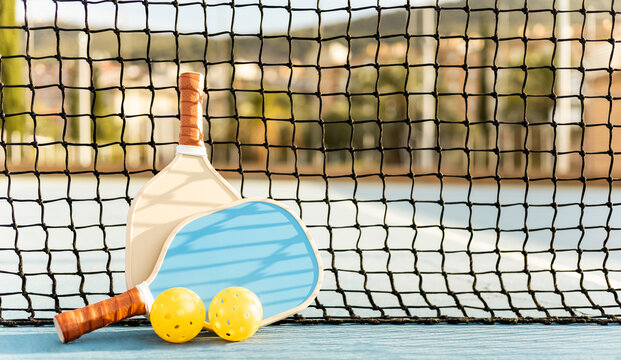 Front view of two pickleball rackets and two balls resting on a net of a sports court.Pickle ball concept.Copyspace for ad advertising.