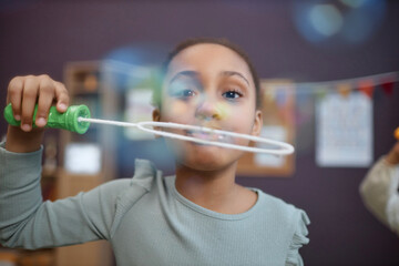 Portrait of cute Black girl playing with soap bubbles in preschool and looking at camera