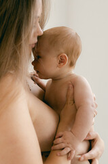 Nude woman with baby in her arms on lighte background. Happy motherhood and breastfeeding concept. Photos with soft focus. Good morning concept. Cute naked baby looking at the camera