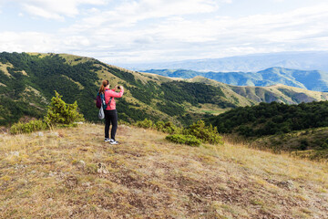 Naklejka na ściany i meble Woman hiker walking on a scenic mountain landscape, taking photos, enjoying leisure activity.