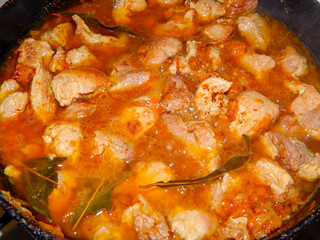 pork meat with spices, onions and carrots in a frying pan is stewed close-up