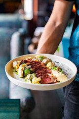 waiter hold sliced beef steak rare with green broccoli