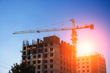 Fototapeta premium construction of a residential building with a construction crane on a construction site against the background of sky with sun