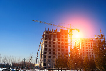 construction crane is building a house on background of a blue sky with sun