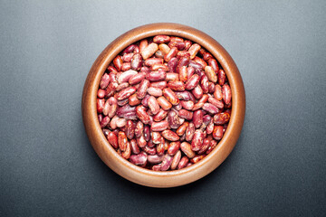 dried red speckled kidney beans in a wooden bowl on black background, top view