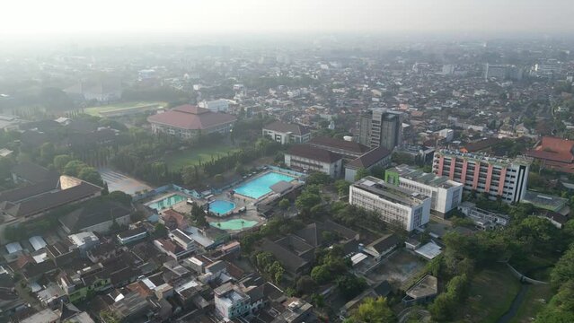 Aerial view of Jogja City with dense buildings development, crowded vehicles traffic in morning sunlight with smog or fog. Population density is displacing agricultural land and forests. Air Pollution