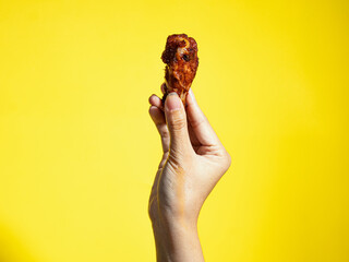 A hand is holding a piece of grilled chicken wing, isolated against a yellow background.