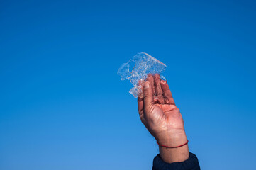 man's hand holds a piece of ice in winter against a blue sky background