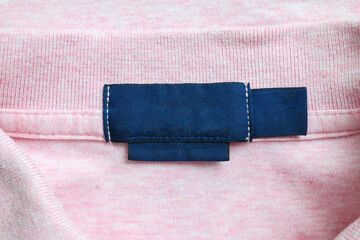 Blank blue laundry care clothes label on pink shirt fabric texture background