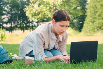 Teenage schoolgirl studying reading her books, tablet and notebook, sitting outdoors. Back to school. Student girl lying on the green grass using laptop in the college yard or park. Distance learning.