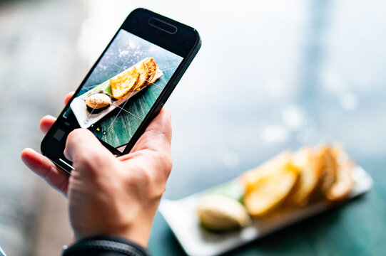 hand with smartphone photographing food at restaurant or cafe