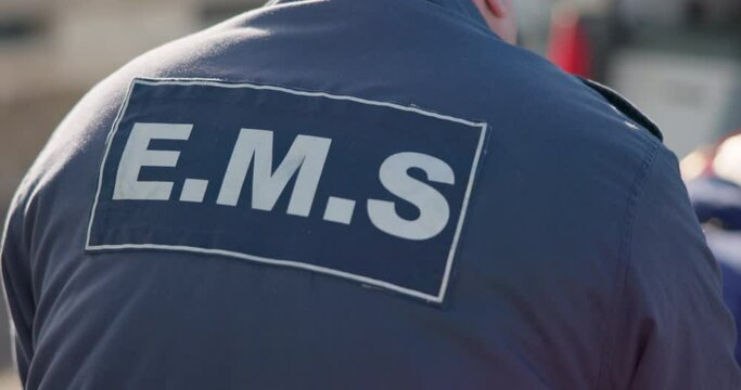 Man, back and ems paramedic in emergency, ambulance and working in healthcare, service in city. Uniform, rear view and person with first aid, help and walking to transport with medical jacket