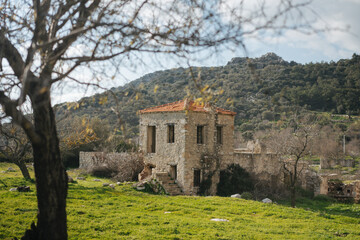 Fototapeta na wymiar An ancient abandoned two-story stone house in a field with a mountain in the background