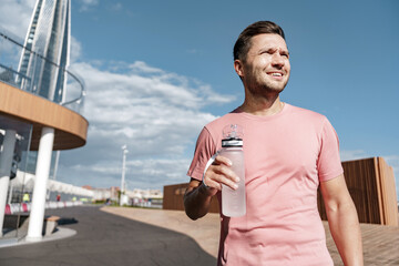 A sports person is a runner who drinks water from a bottle before a warm-up. Getting ready to start jogging in running shoes.