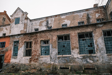Fototapeta na wymiar From below exterior of derelict brick building with crumbling walls located near leafless trees against gray sky