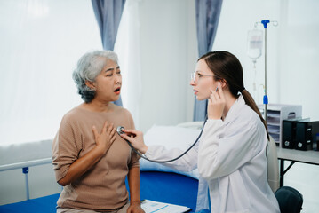 Fototapeta premium Doctor in white suit take notes while discussing and Asian elderly, woman patient who lying on bed with receiving saline solution in hospital or clinic.