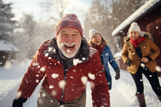 Portrait of happy senior man in winter during snow having fun with family outdoors playing snowballs fight. Active healthy lifestyle in retirement