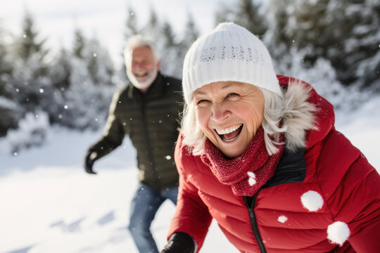 Happy mature couple in winter during snow having fun outdoors in the forest playing snowballs fight. Active healthy lifestyle in retirement
