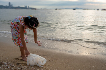 Girl on the beach at dusk cleaning plastic bag. Waste at the sea shore.