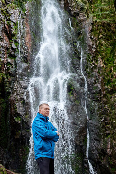 Tourist attraction of Germany - falls of Burgbach Waterfall near Schapbach, Black Forest, Baden-Wurttemberg, Germany. Man hiker in blue jacket standing on stone and looks at flow of falling water