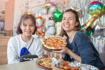 mother and daughter cutting slice of pizza and eating italian pizza together while having enjoying with party to celebrate for weekend in kitchen at home. single mother eats happily with her baby.