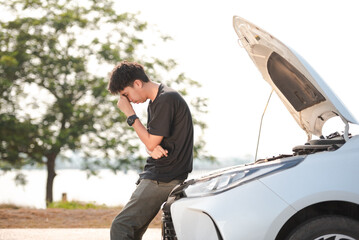 A stressed Asia young man has a problem with his car breaking down. He looked annoyed because the engine has failed.