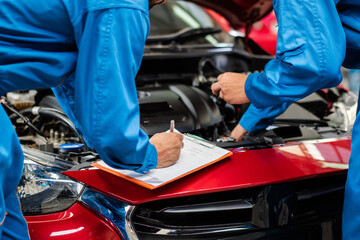 Fototapeta na wymiar Automotive mechanic men with assistant checking damage under-car condition, vehicle maintenance technician write on checklist document in garage at auto repair shop. after service concept