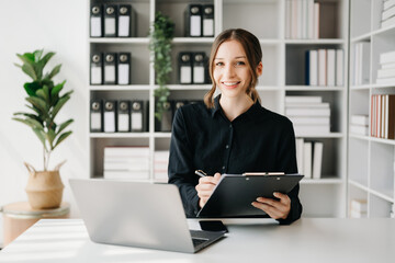 Fototapeta premium Confident business expert attractive smiling young woman typing laptop ang holding digital tablet on desk in office..