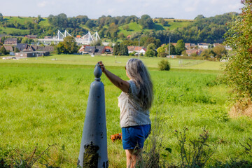 Senior female tourist standing at border marker between Belgium and Holland on Caestert plateau,...