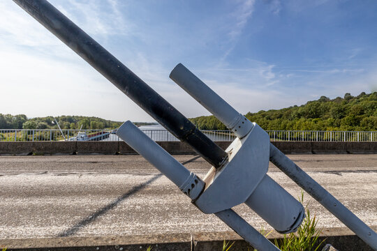 Closeup of huge metal steel anchor of tension cable of Lanaye cable-stayed bridge, rural vehicular road and Albert canal in background, bad asphalt, sunny day in Vise, Belgium