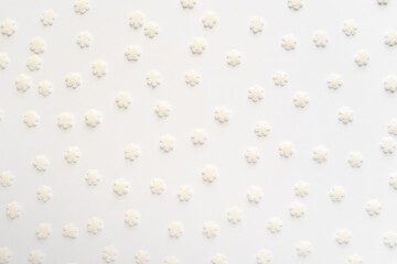 White sugar sweet snowflakes sprinkles on white background. Sweet backing decoration for cake and candy.Copy space. 